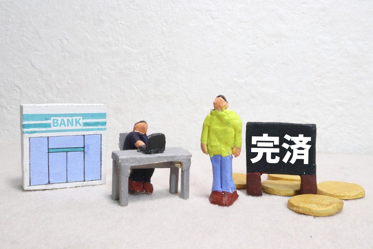 「完済」と書かれた札と、銀行・人物のミニチュア