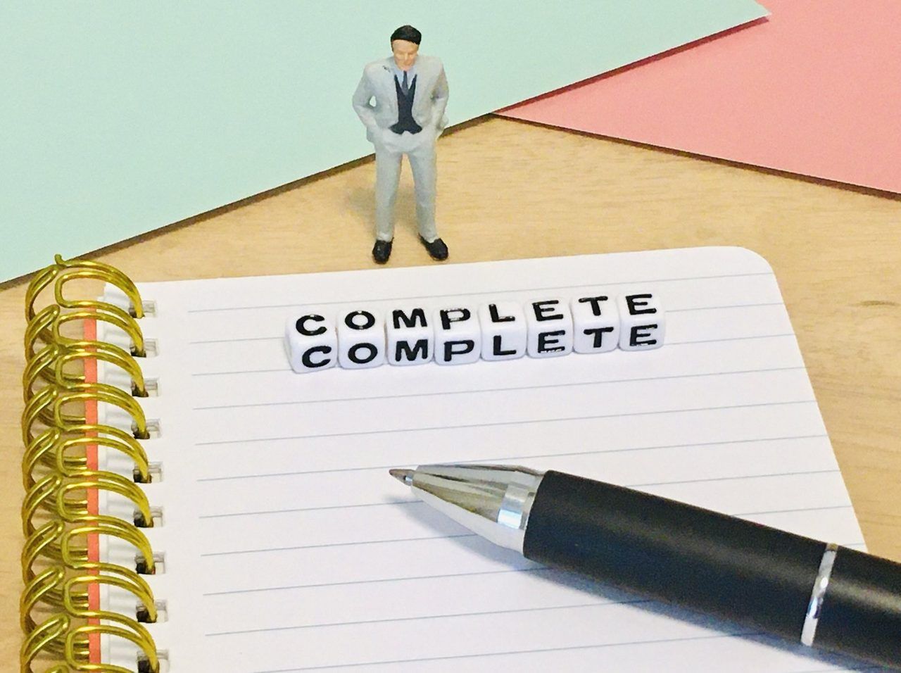 「COMPLETE」の文字とペン、スーツ姿の人形
