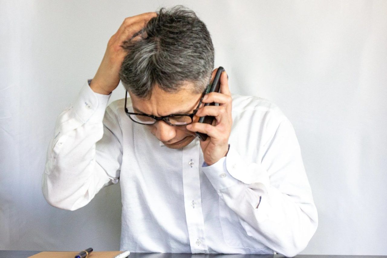 電話をしながら、頭を抱えて悩む男性