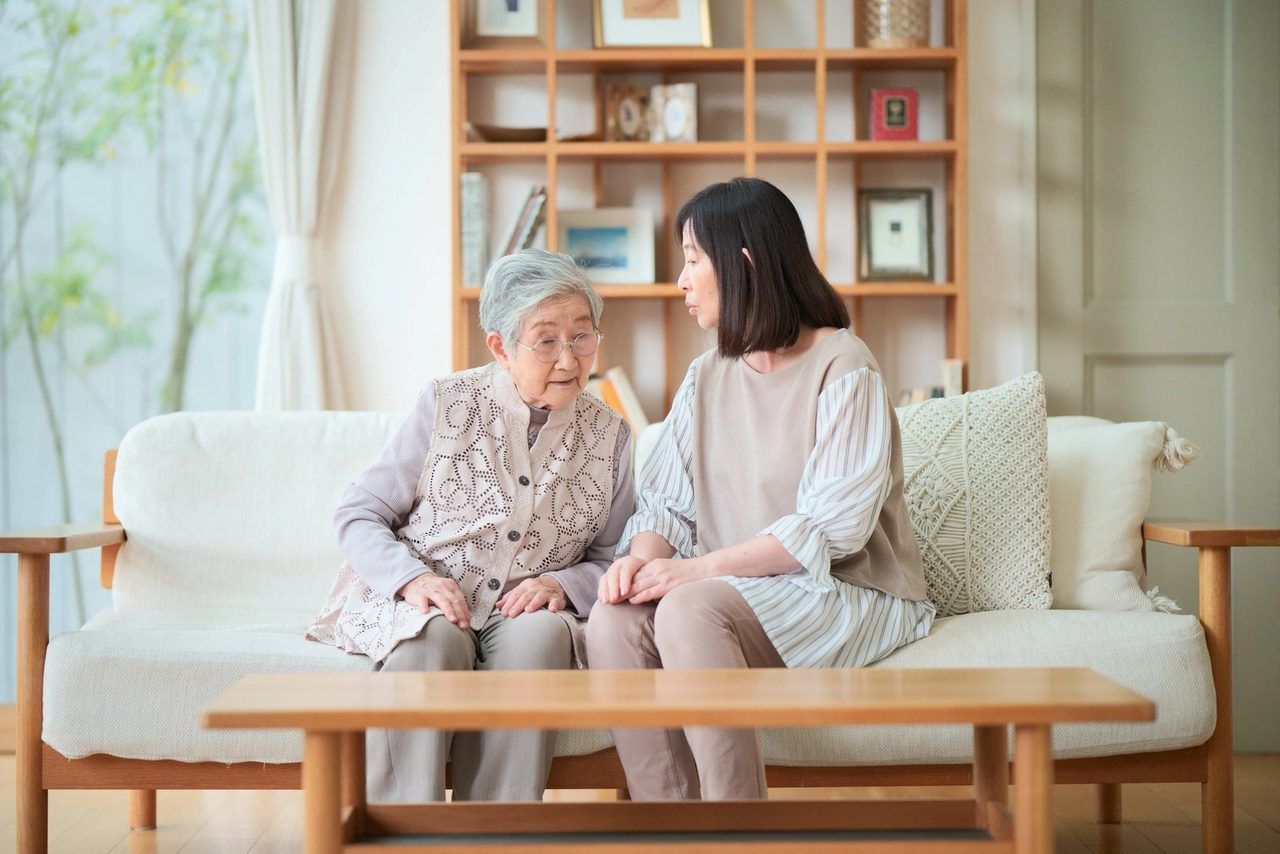 ソファで寄り添って話す、ご高齢の女性と娘さん