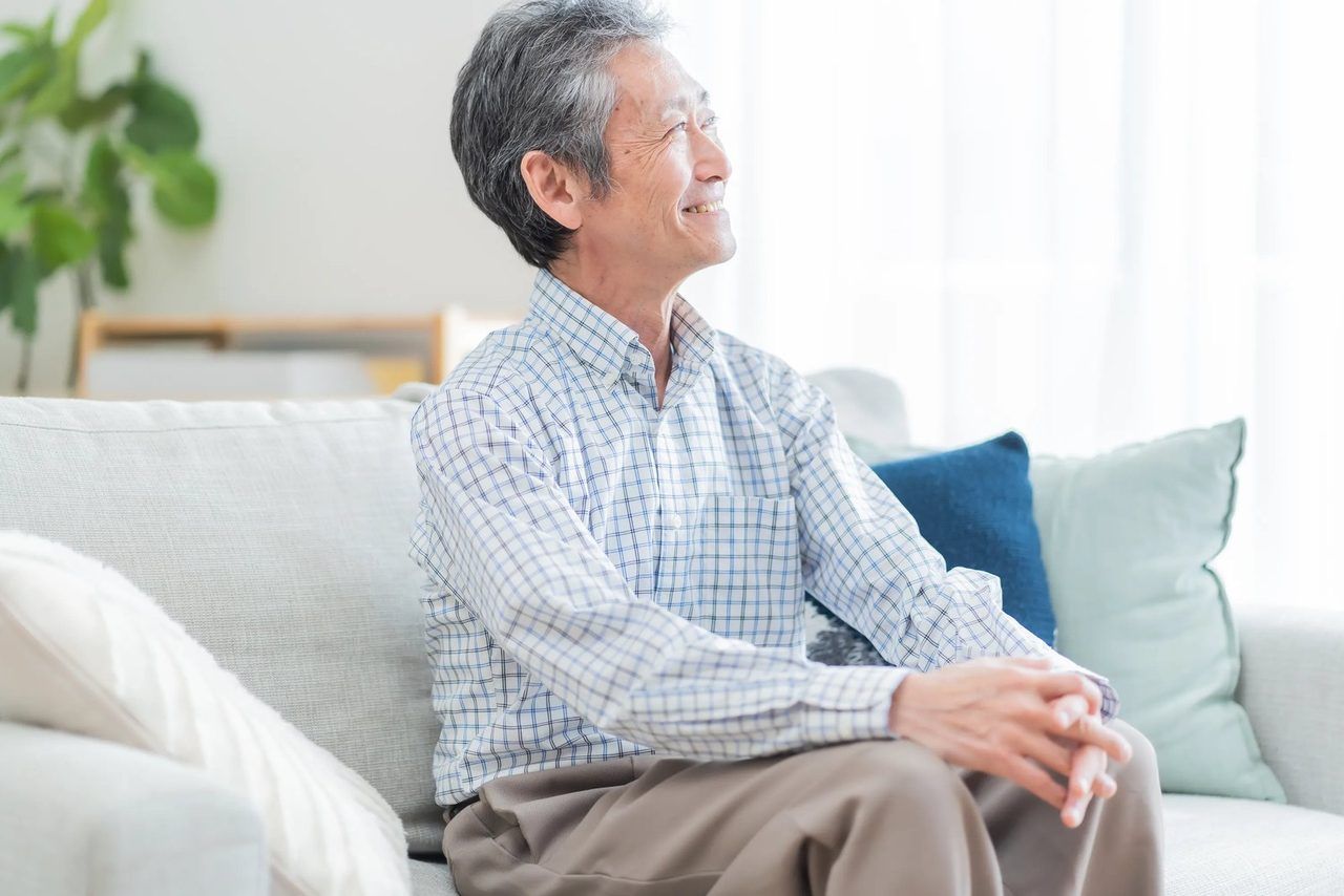 ソファでくつろぎ、穏やかに笑うご高齢の男性