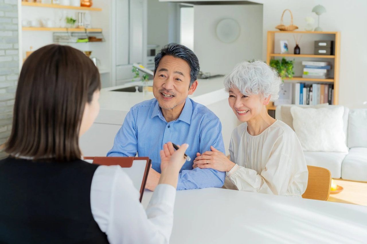 おうちのリビングで、ご高齢のご夫婦が女性スタッフに相談している場面