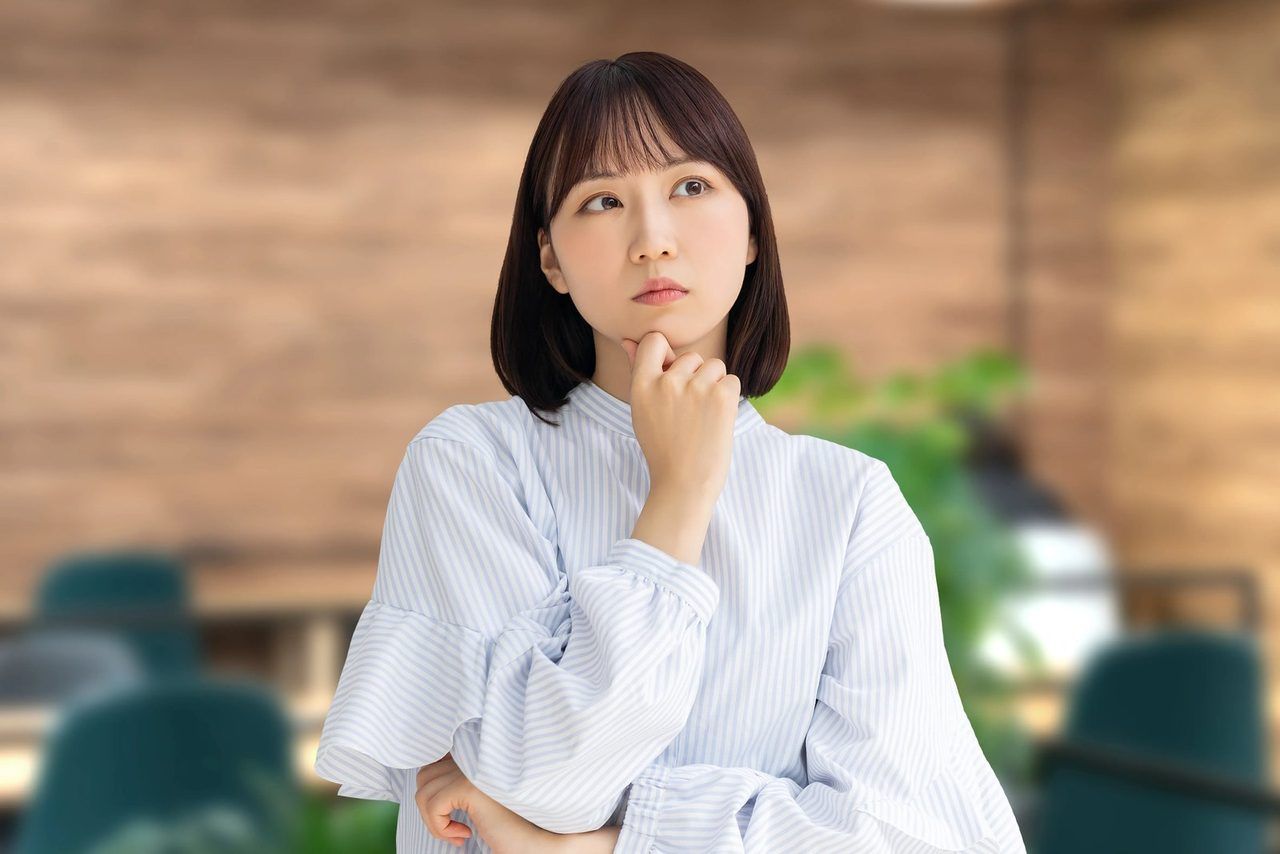 木の壁の前で、考えごとをする女性