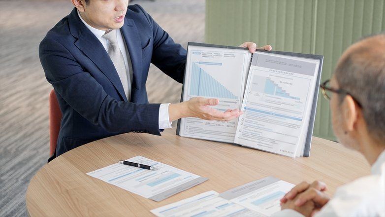 男性スタッフが、資料を開いてご高齢の男性に説明している場面