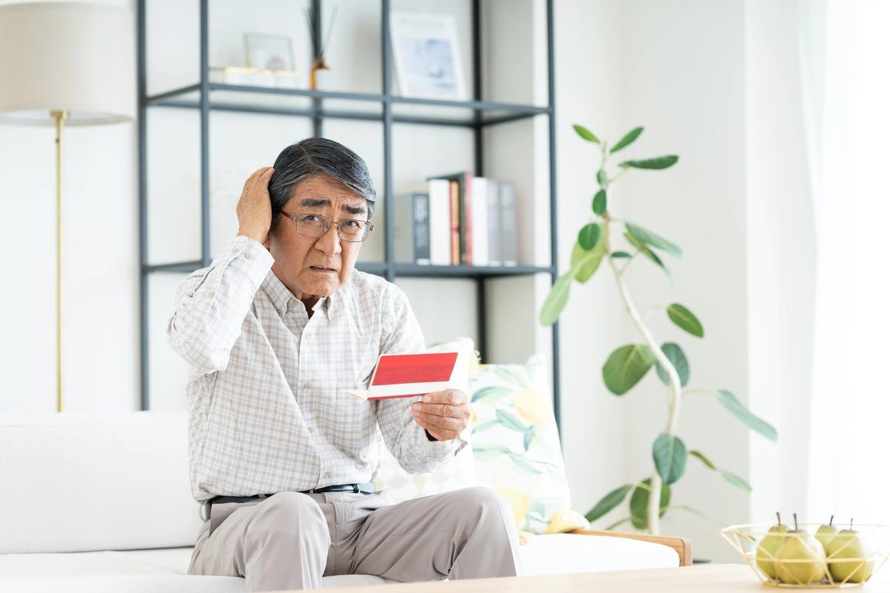 赤い手帳を手に、困った表情で考え込む男性