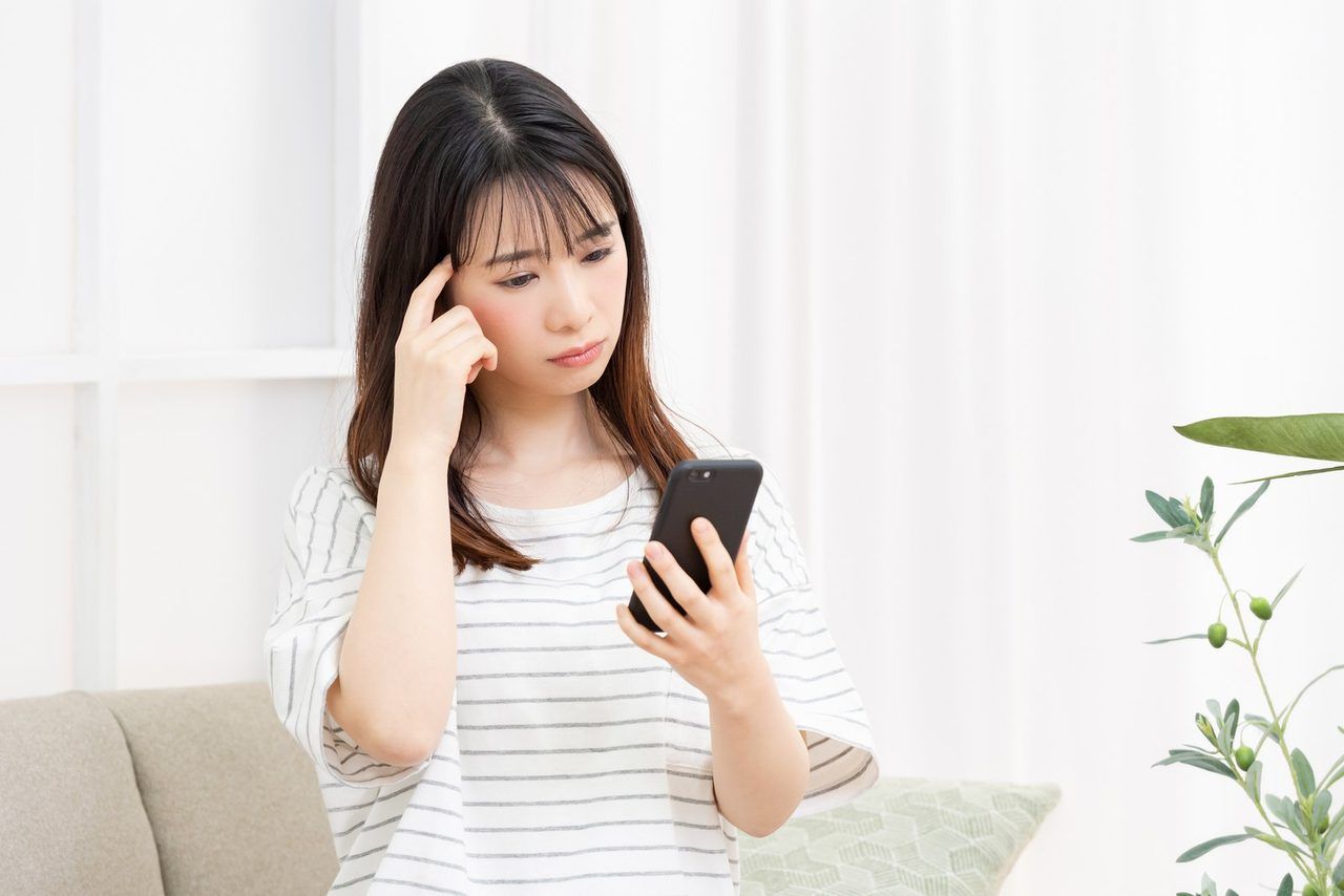 スマートフォンを見て、悩んでいる女性