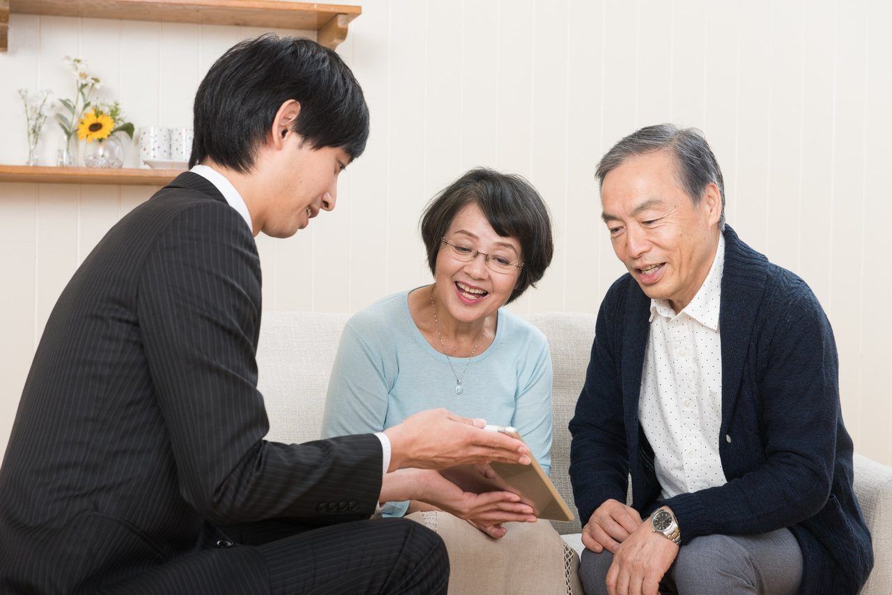 スーツの男性が、ご高齢のご夫婦にタブレットを見せて説明する場面