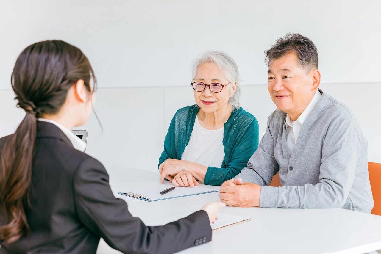 女性スタッフが、ご高齢のご夫婦に資料を見せながら説明している場面